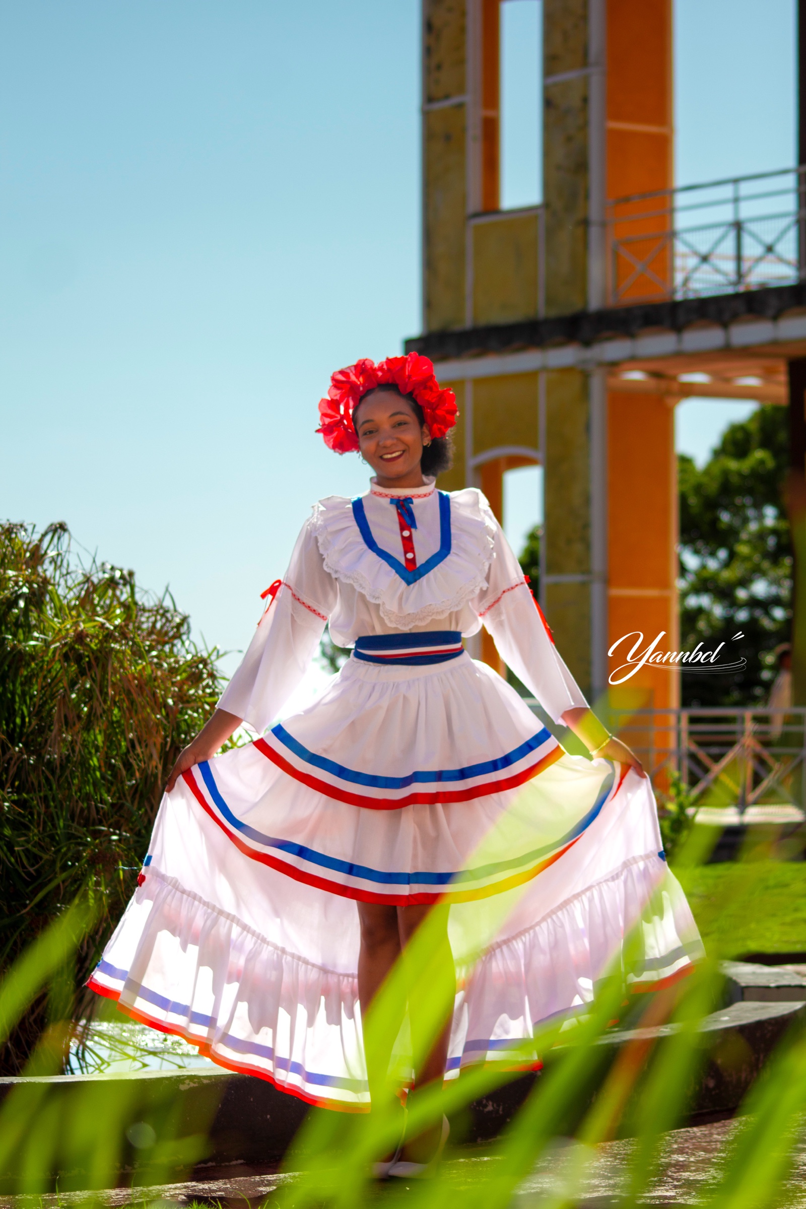 Femme en tenue traditionnelle posant devant une architecture guadeloupéenne
