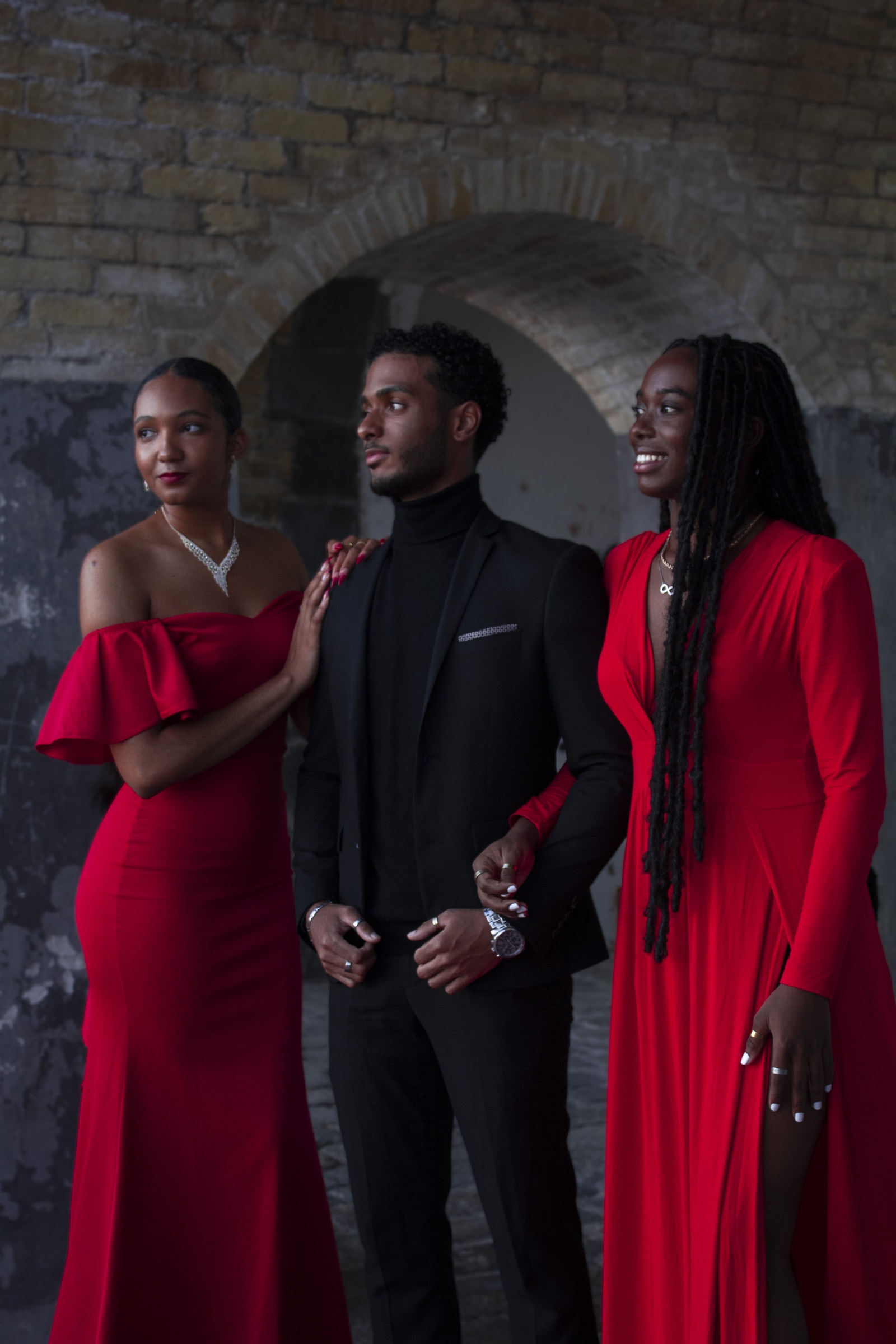 Trois modèles en tenues rouge et noire posent sous les arches d’un bâtiment historique