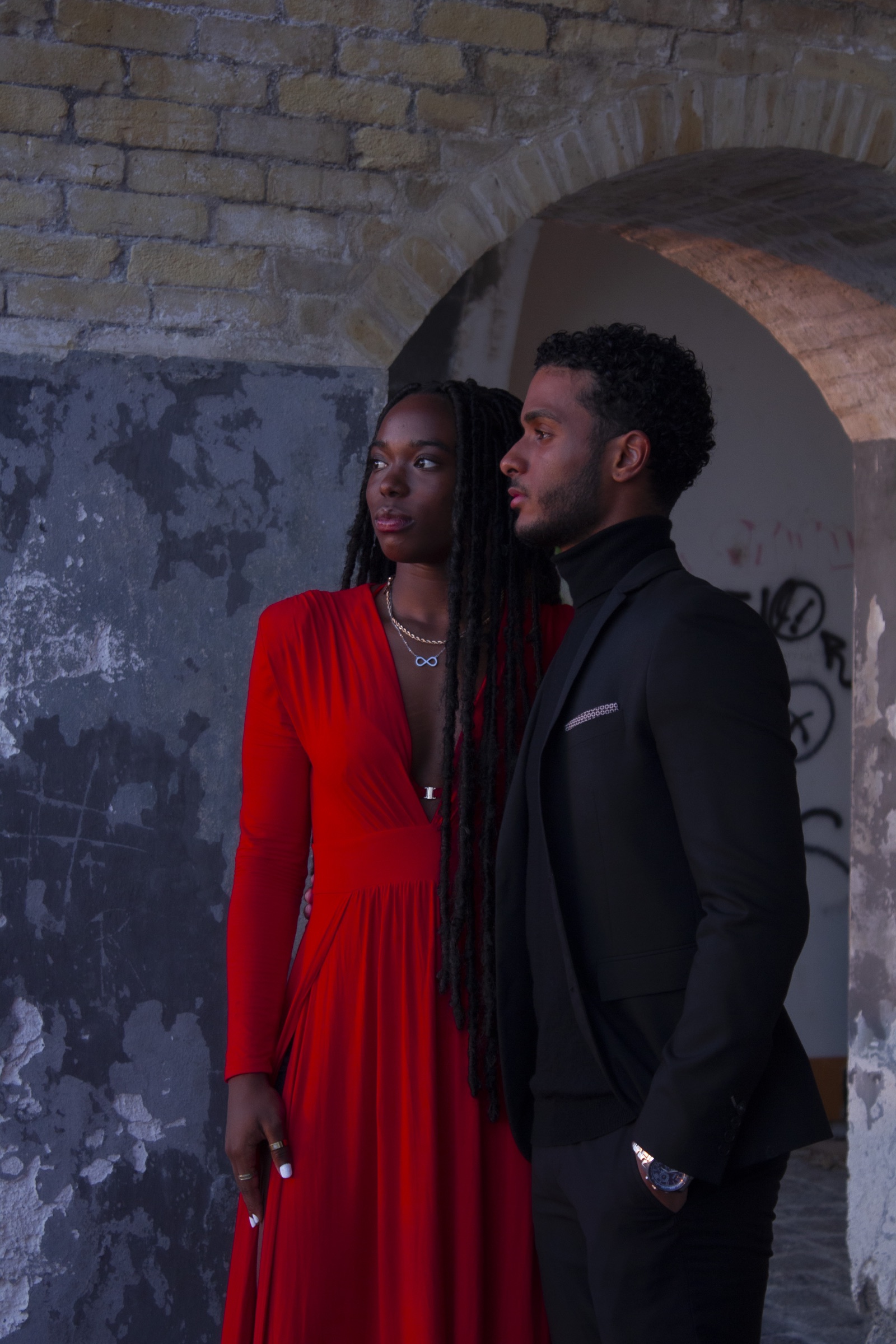 Un couple en rouge et noir pose sous une arche ancienne